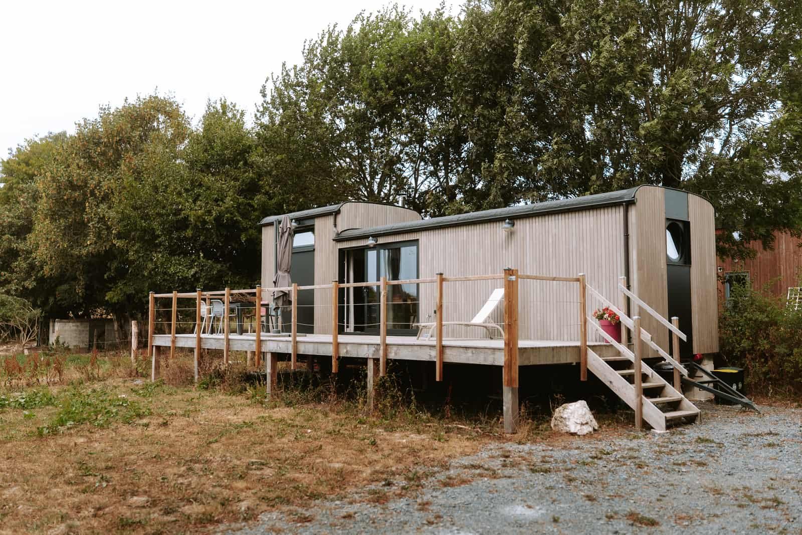 Façade en bois de la Tiny House d'Habaru entourée d'arbres, terrasse et escalier d'accès